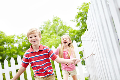 Buy stock photo Happy children, siblings or playing with stick in garden for summer together in nature or backyard. Young, brother and sister running with smile for fun childhood, bonding or holiday weekend by fence