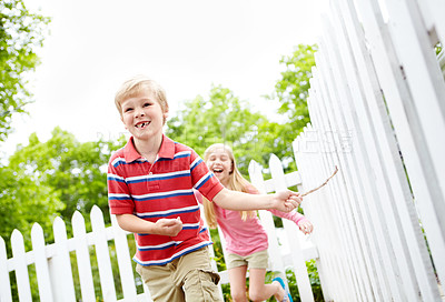 Buy stock photo Happy kids, siblings or playing with stick in garden for summer together in nature or backyard. Children, brother and sister running with smile for fun childhood, bonding or holiday weekend by fence