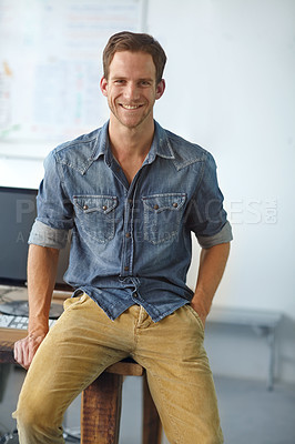 Buy stock photo A young casual businessman sitting on his desk in his office