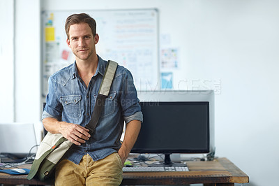 Buy stock photo A handsome young man with a satchel leaning against a table in his office