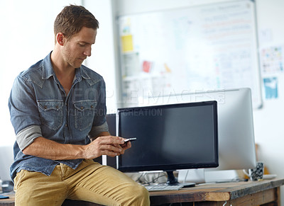 Buy stock photo A young man sitting on his desk at work while reading a text message