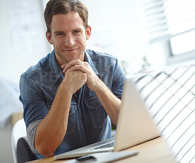 Buy stock photo A young man sitting at his desk while looking at the camera