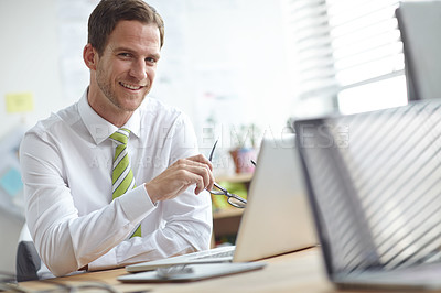 Buy stock photo A handsome young businessman sitting at his desk while smiling at the camera