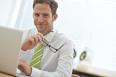 Buy stock photo A young businessman smiling from behind his laptop