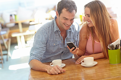 Buy stock photo A happy young couple sitting in a coffee shop reading a text message and smiling