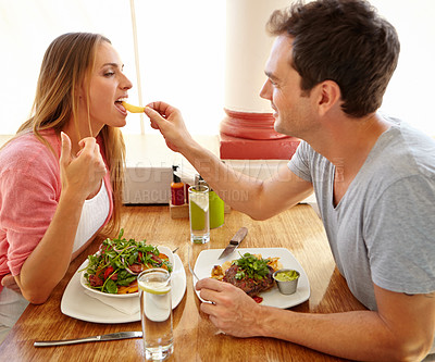 Buy stock photo A handsome young man giving his girlfriend a taste of his food while they have lunch together in a restaurant