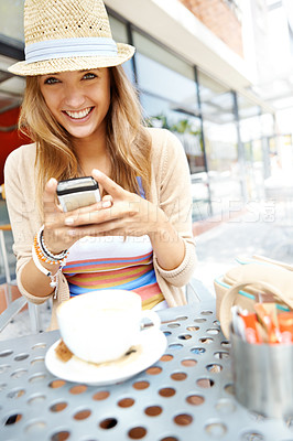 Buy stock photo A casual young woman sending a text message while sitting at a sidewalk cafe in the city - portrait