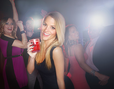 Buy stock photo A lovely young blonde woman smiling at the camera while standing on the dancefloor holding a cocktail