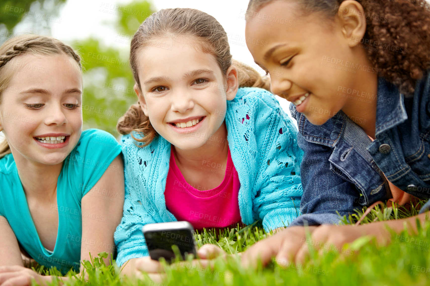 Buy stock photo Three happy young girls sitting outside texting on a cellphone 