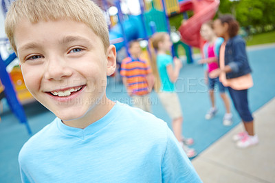 Buy stock photo A young boy smiling at the camera while his friends play in a playground behind him