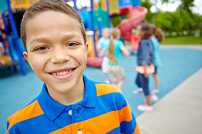 Buy stock photo A young African-American boy smiling at the camera while his friends play in a playground behind him