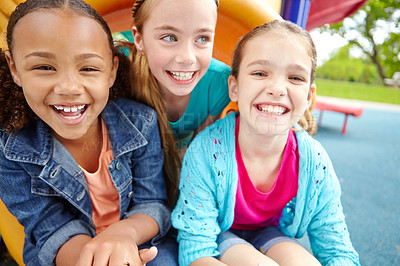 Buy stock photo Three happy young girls sitting on a slide in a playpark