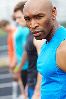 Buy stock photo Close up side view of a male runner looking at the camera with a line up of competitors blurred in the background
