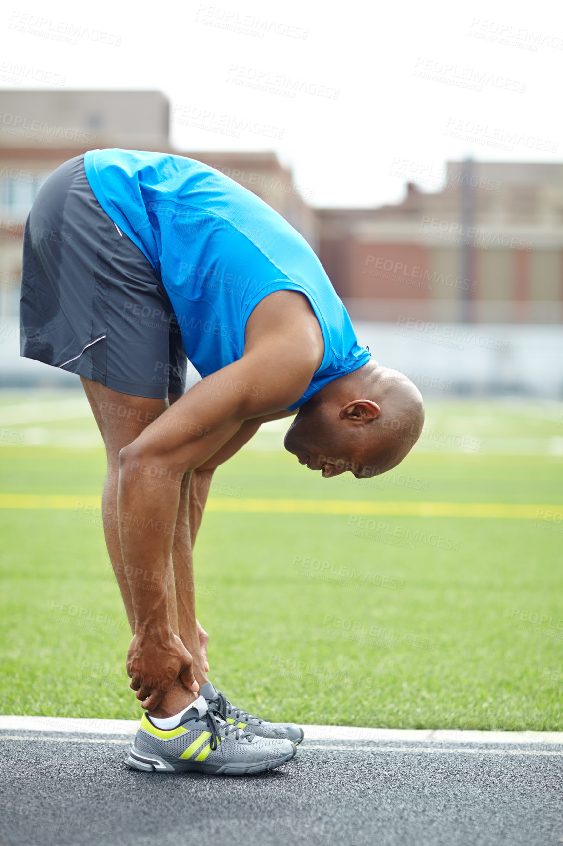 Buy stock photo Side view of a male athlete stretching his leg muscles at the race track