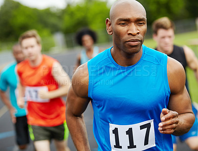Buy stock photo Front view of a male runner looking determined while running in a race with other athletes in the background