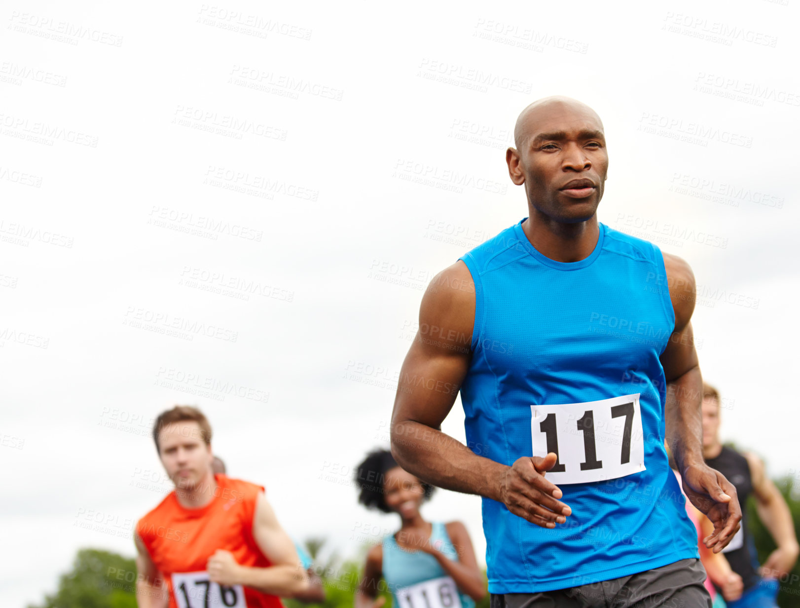 Buy stock photo Cropped front view of a determined male athlete with competitors in the background