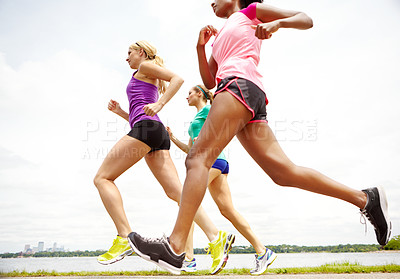 Buy stock photo Cropped side view of a group of athletes jogging beside a lake