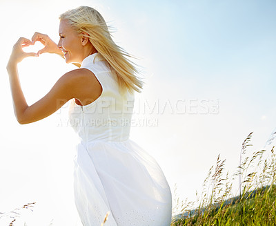 Buy stock photo A young woman making a heart gesture in a field