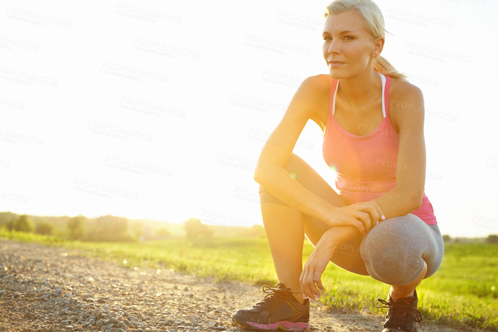 Buy stock photo A beautiful young woman in sportswear crouching on a dirt road