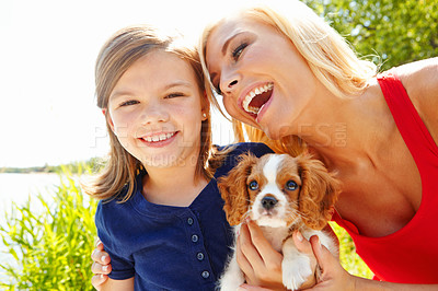 Buy stock photo Portrait of a little girl holding a puppy while her mother smiles at her lovingly 