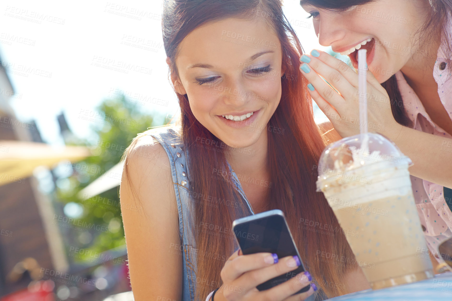 Buy stock photo A teenage girl texting on a cellphone while her friend whispers something in her ear