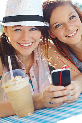 Buy stock photo Two adolescent girls sharing earphones while listening to music on a mobile phone