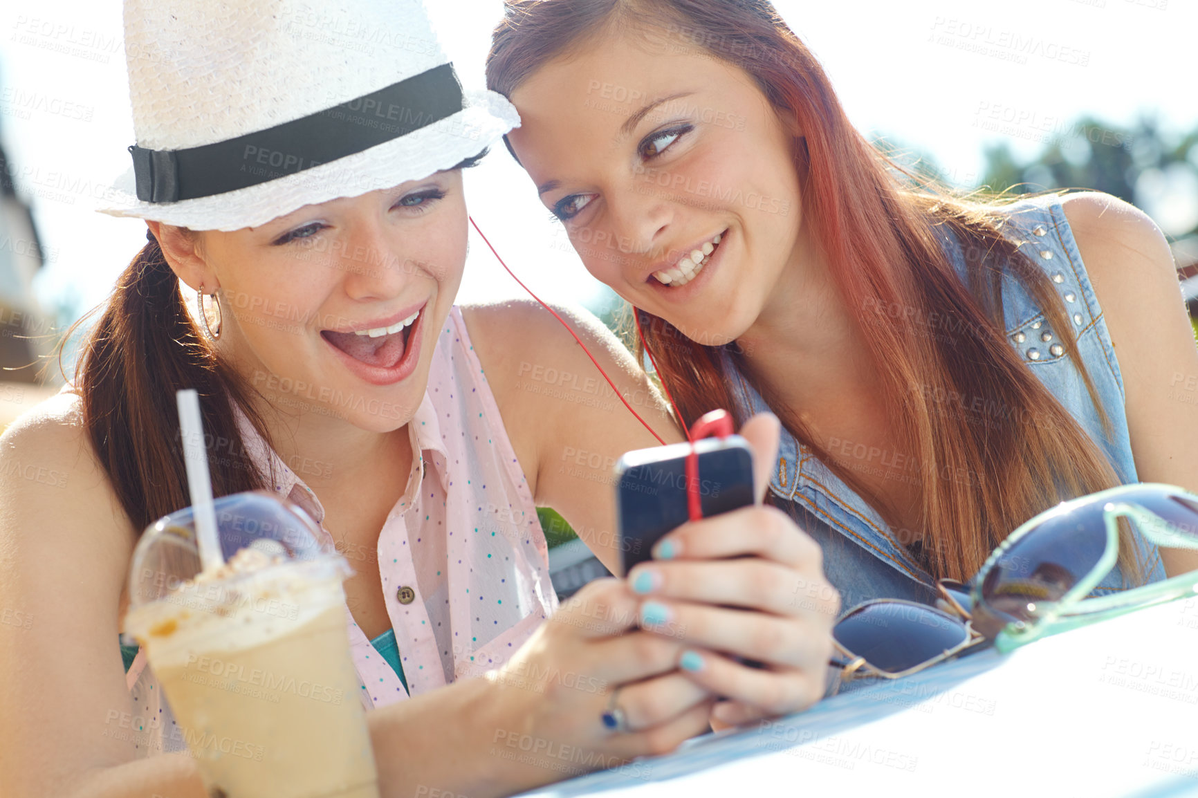 Buy stock photo Two adolescent girls sharing earphones while listening to music on a mobile phone