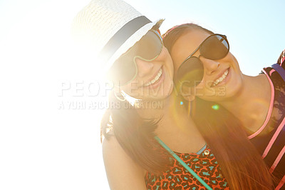 Buy stock photo Low angle view of two teenage girls standing with their arms around each other against a sunny sky