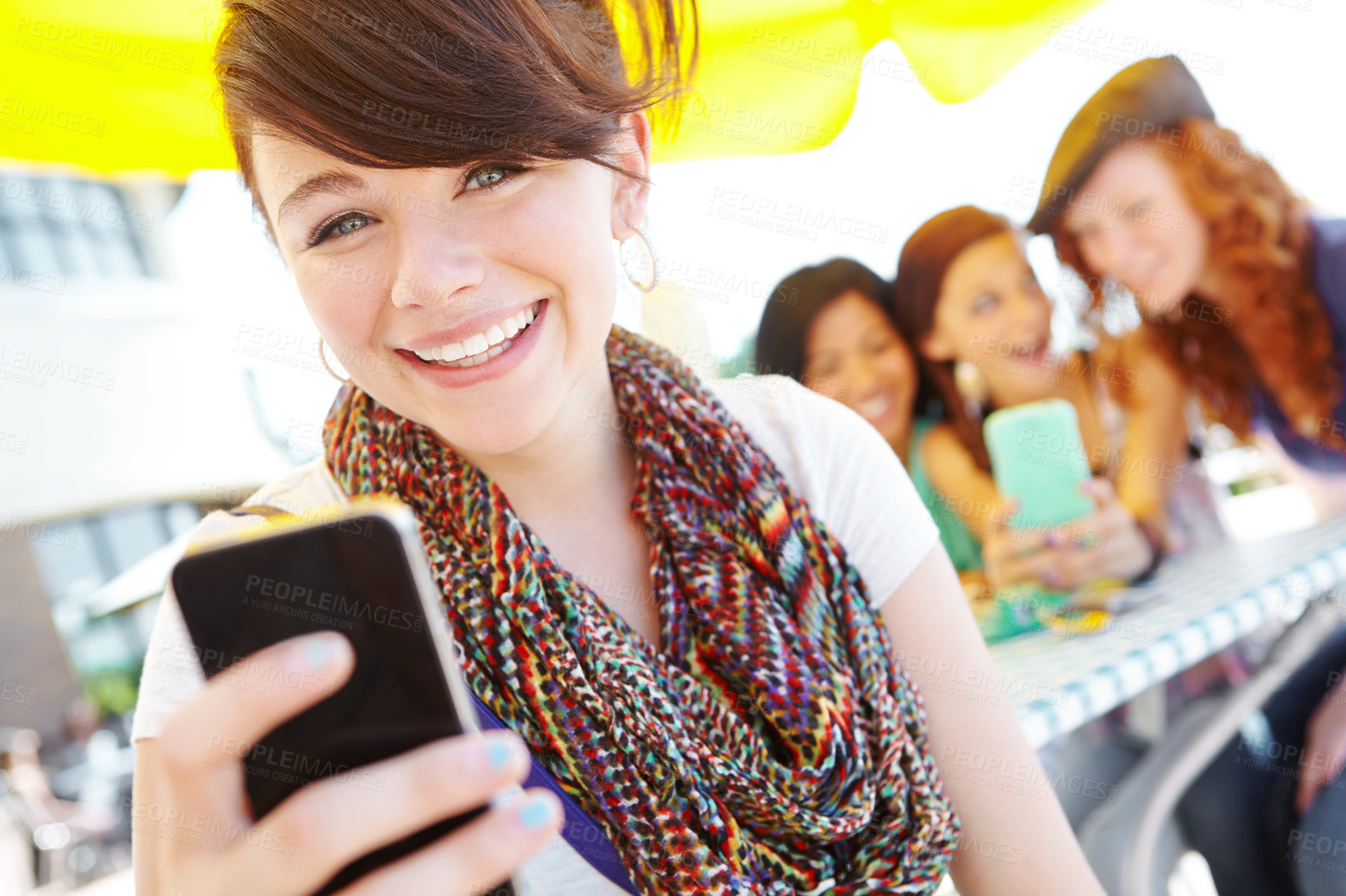 Buy stock photo A beautiful young adolescent girl holding a cellphone with her friends in the background