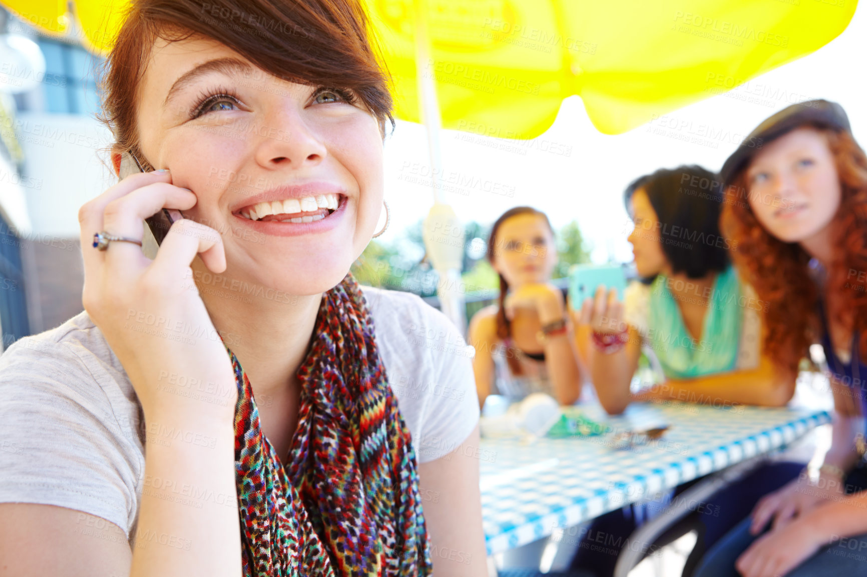 Buy stock photo An adolescent girl smiling while she speaks on her cellphone with her friends in the background