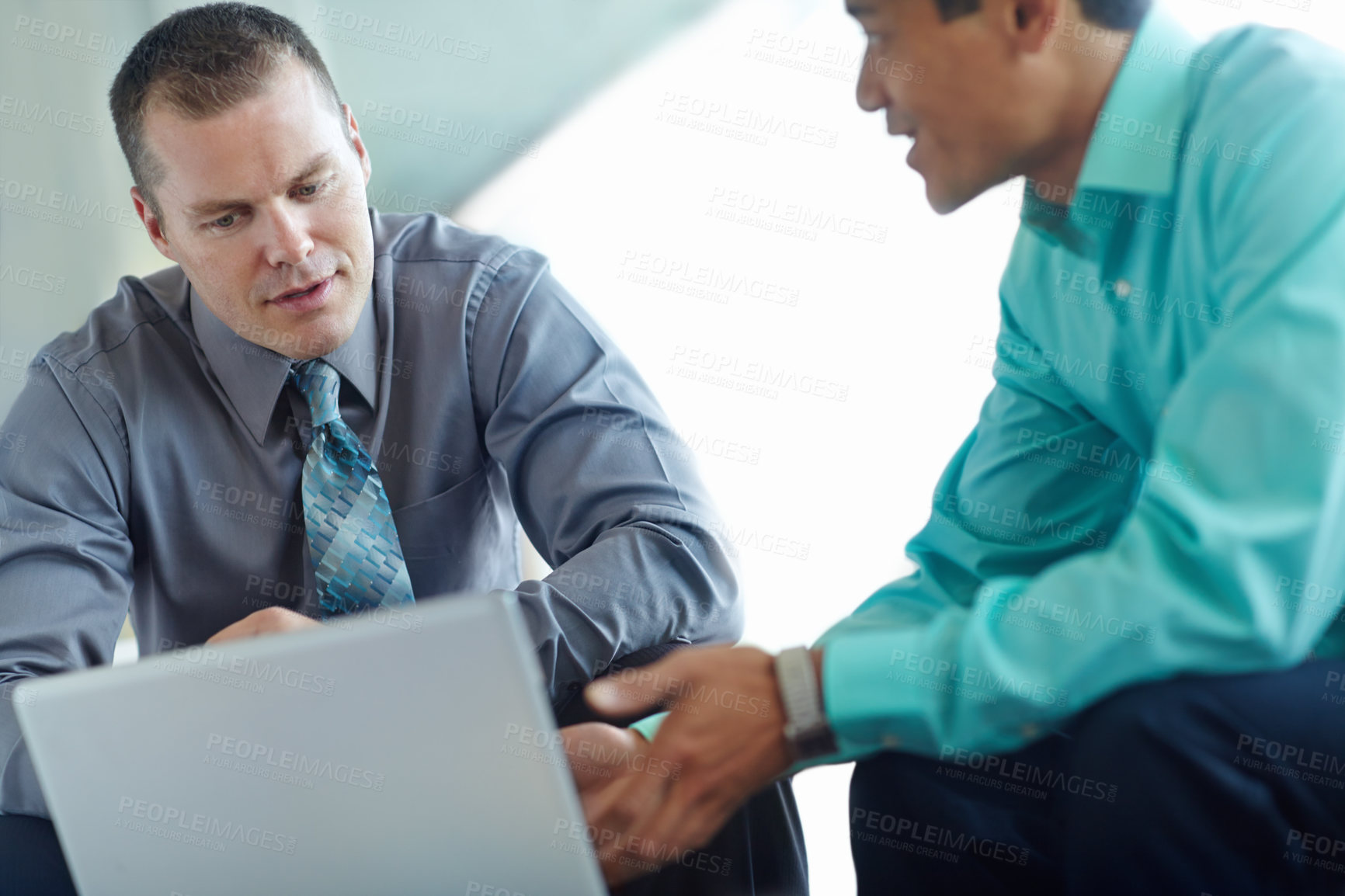 Buy stock photo Two handsome young businessmen working together while sharing a laptop between them