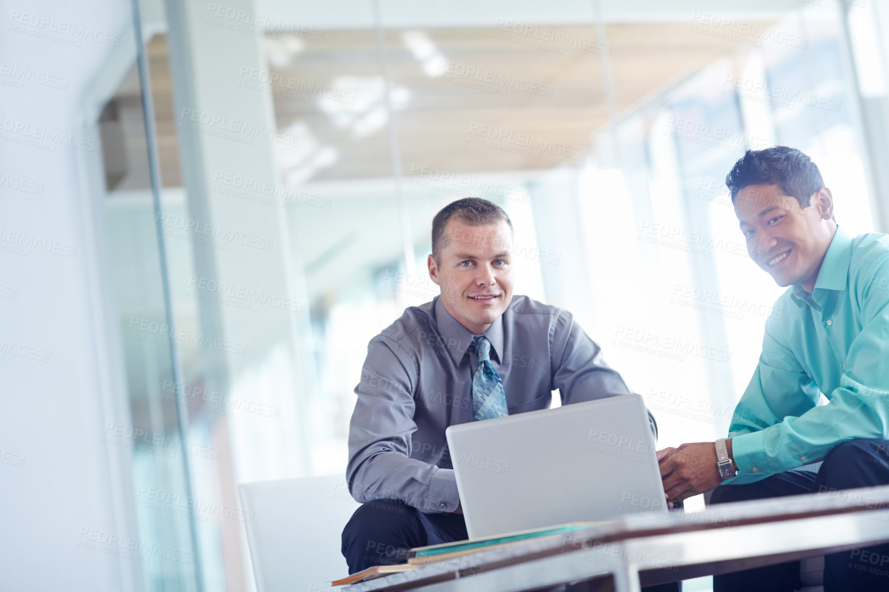 Buy stock photo Two handsome young businessmen working together while sharing a laptop between them