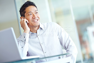 Buy stock photo An ambitious young businessman taking a call while working on his laptop