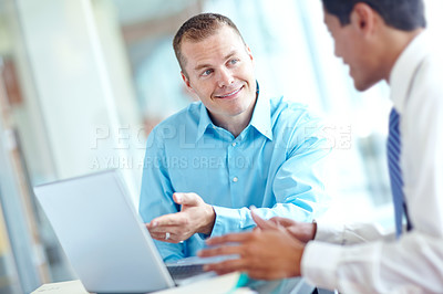 Buy stock photo Two handsome young businessmen working together while sharing a laptop between them