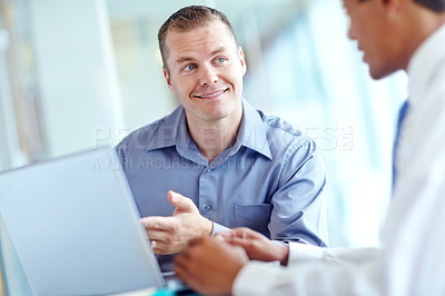 Buy stock photo Two handsome young businessmen working together while sharing a laptop between them