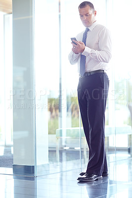 Buy stock photo A serious caucasian businessman using his smartphone while working