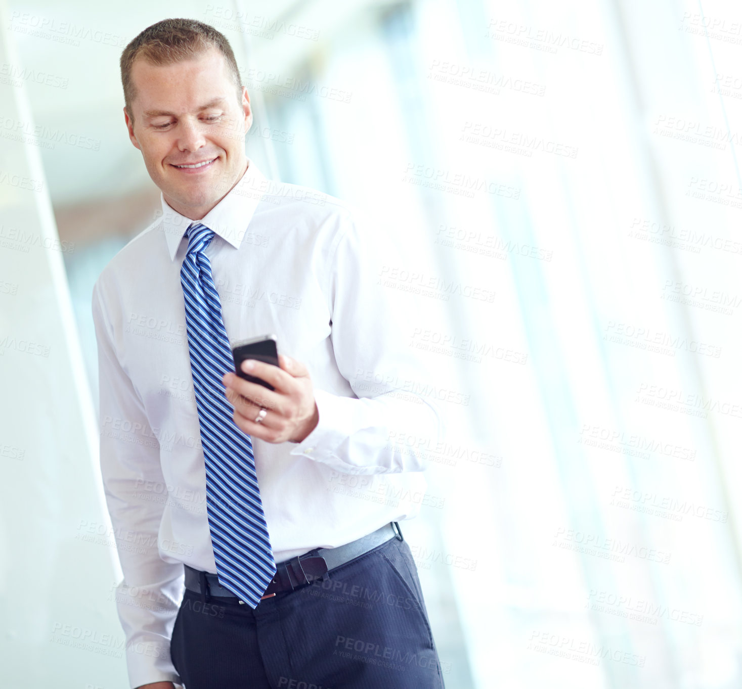 Buy stock photo A smiling caucasian businessman using a smartphone wile working