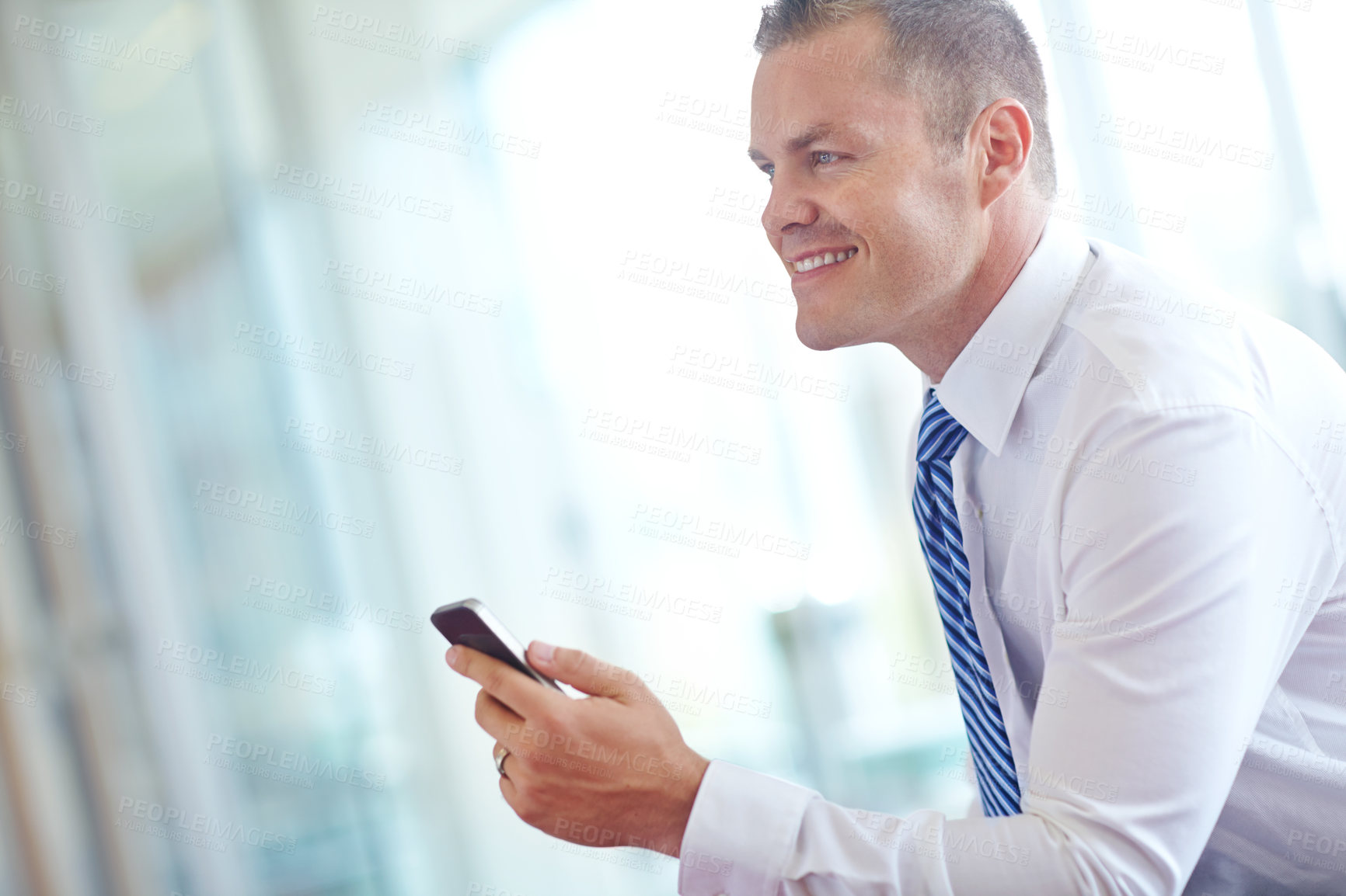 Buy stock photo A smiling caucasian businessman using a smartphone wile working