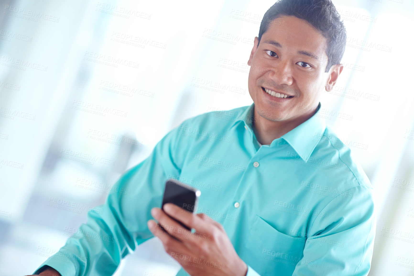 Buy stock photo A smiling asian businessman using his mobile while working