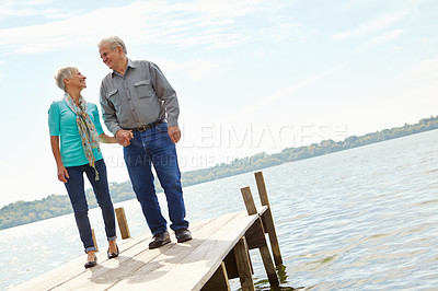 Buy stock photo A loving elderly couple looking at each other while standing on a jetty