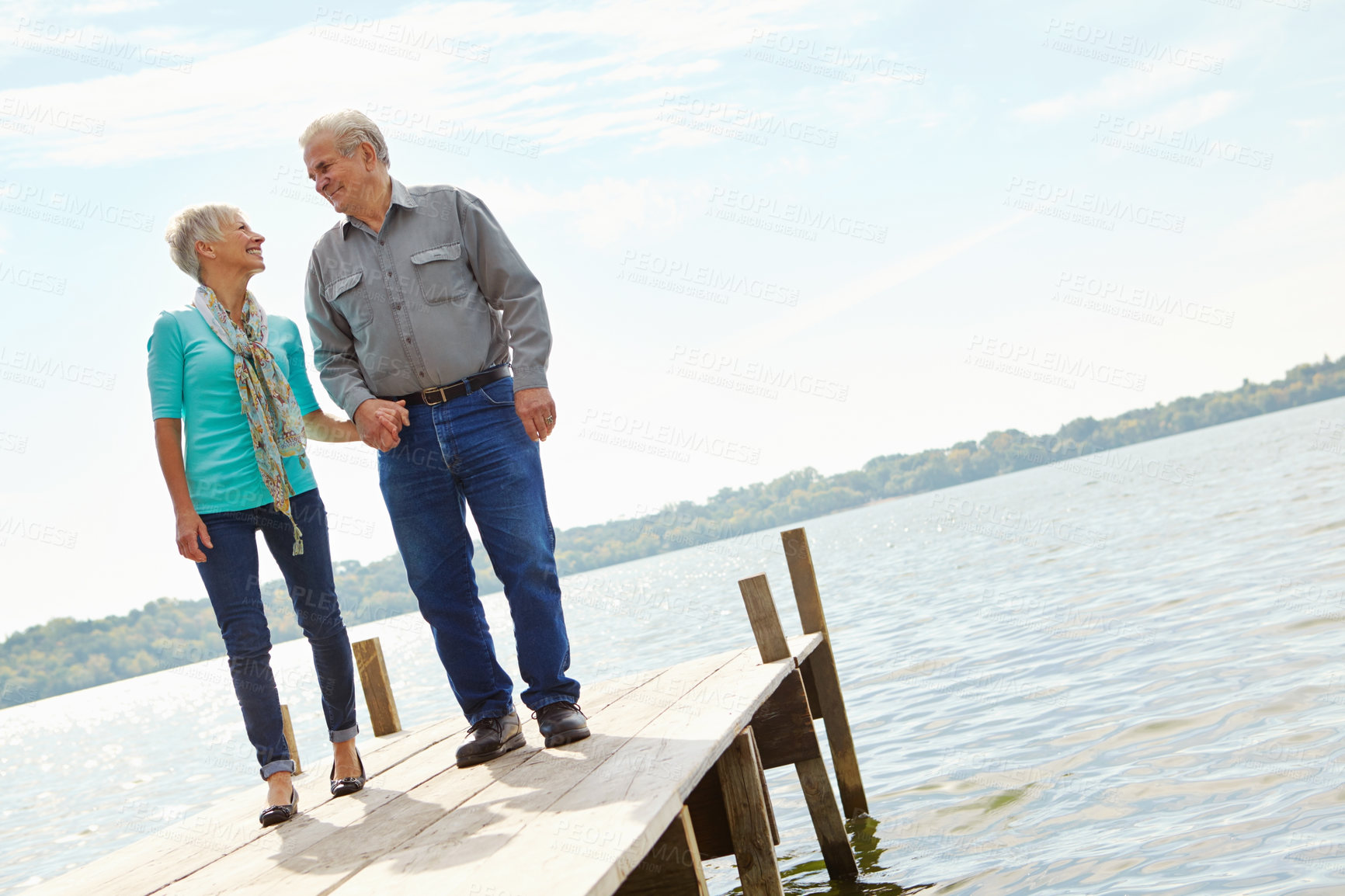 Buy stock photo A loving elderly couple looking at each other while standing on a jetty