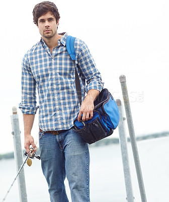 Buy stock photo A handsome young fisherman strolling near the lake while carrying his gear