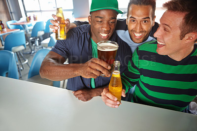 Buy stock photo Three guy friends clinking their beer bottles and glasses at the bar