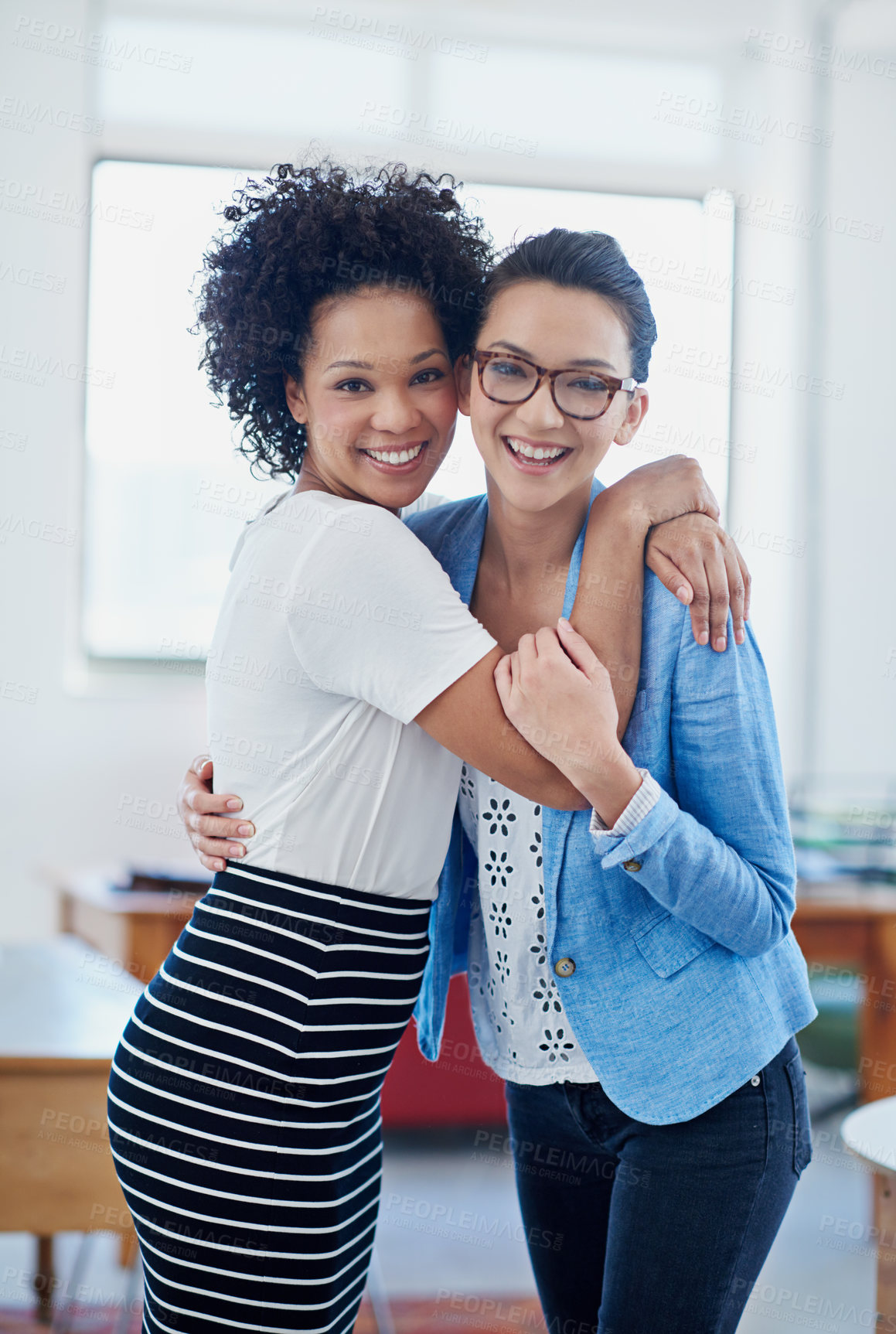 Buy stock photo Portrait of two female coworkers embracing happily in an office