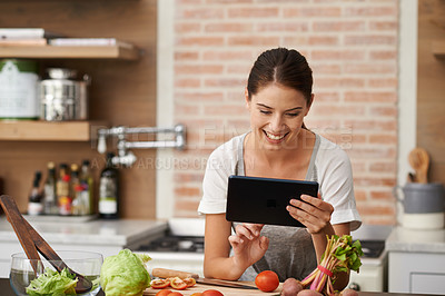 Buy stock photo Shot of an attractive young woman using her tablet in the kitchen