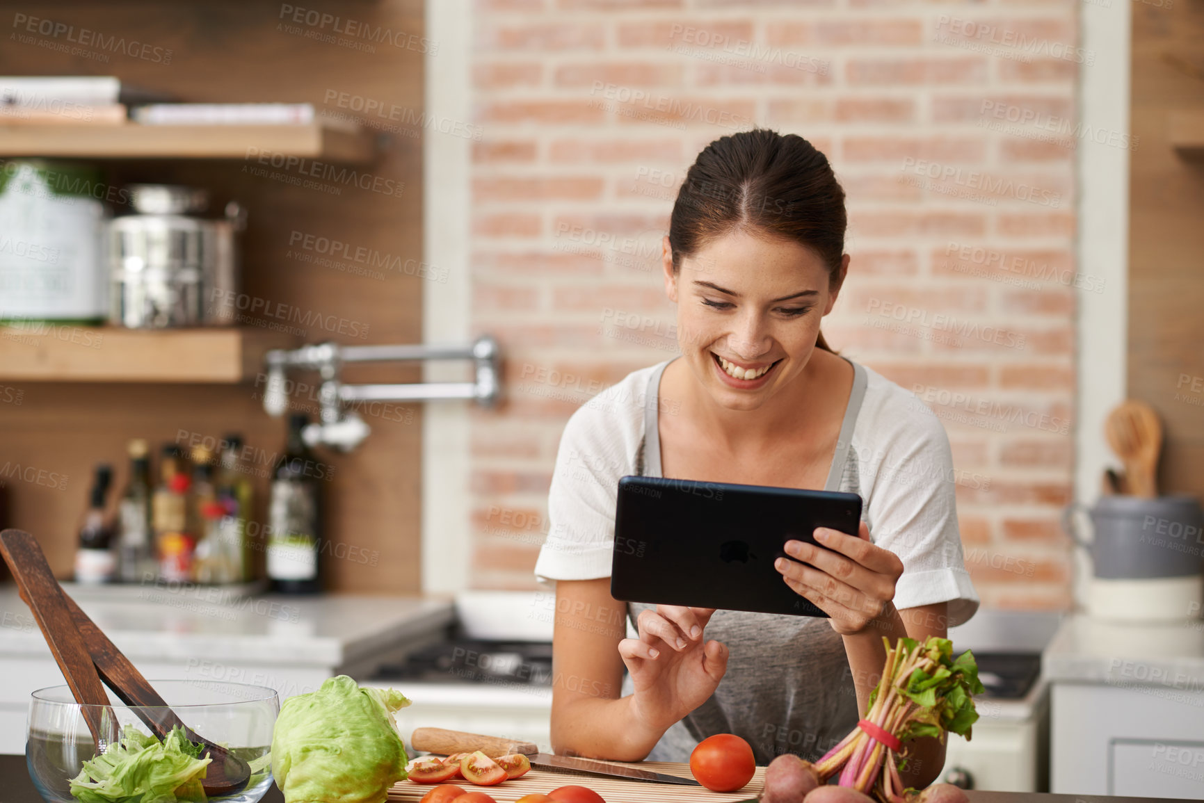 Buy stock photo Shot of an attractive young woman using her tablet in the kitchen