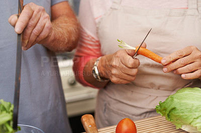 Buy stock photo Closeup of the hands of two people preparing or cooking a meal in the kitchen. Senior romantic couple cutting carrots with a knife and preparing a healthy vegetarian salad together for lunch at home