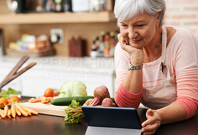 Buy stock photo Shot of a woman resting her chin on her hands as she watches a tablet in her kitchen 