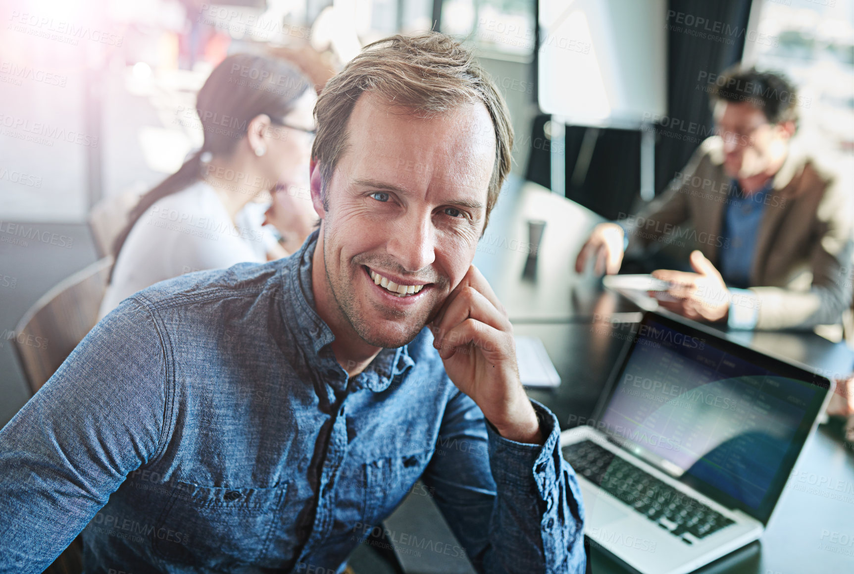 Buy stock photo Portrait of a smiling businessman sitting at a boardroom table with colleagues in the background