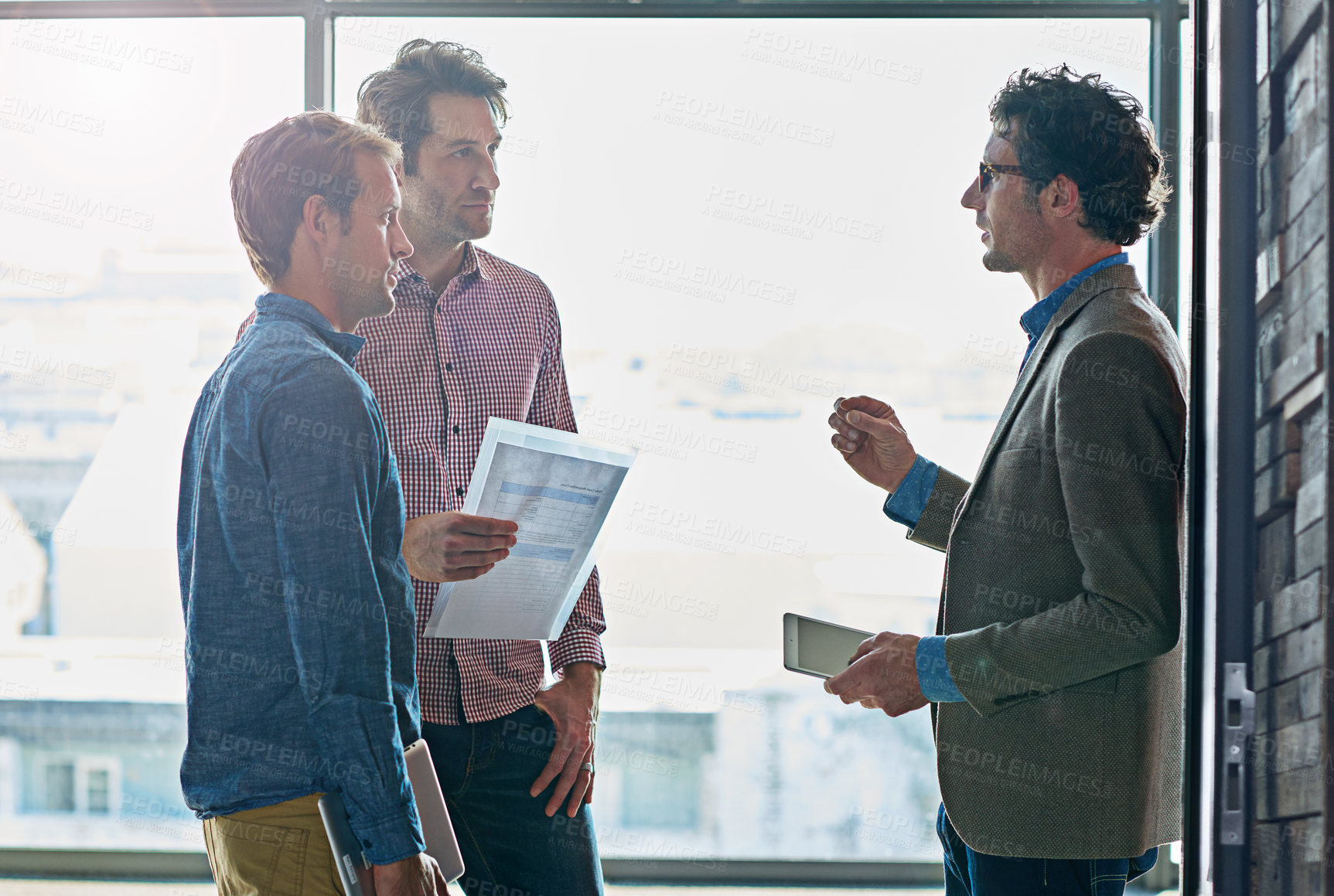 Buy stock photo Business people, men and teamwork with discussion for planning by window of office for b2b brainstorming. Collaboration, employees and tablet with document for financial review and project report